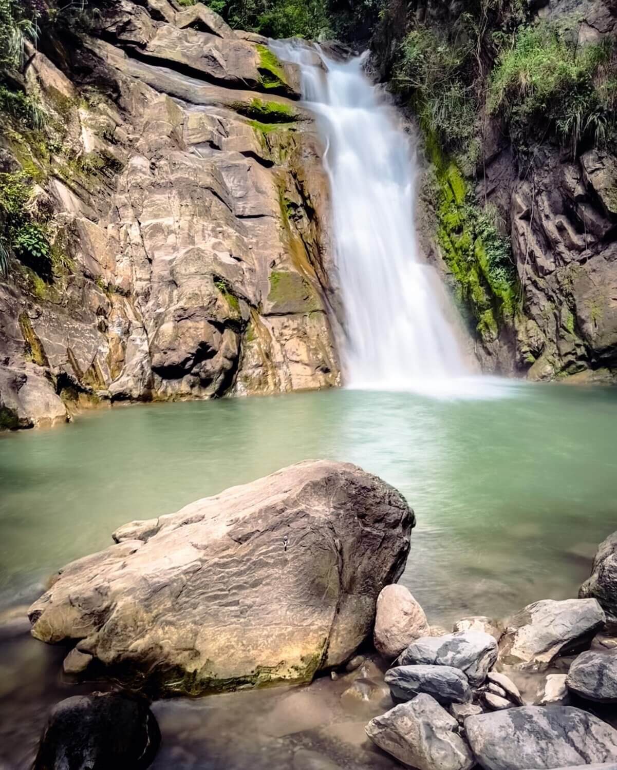 Cascada de los Saltos del Mico en Villeta, rodeada de rocas y vegetación, con agua cristalina cayendo sobre una poza natural