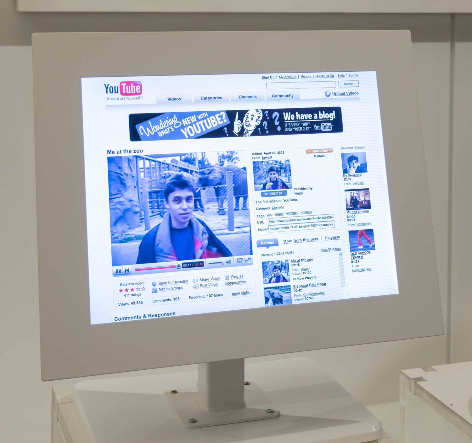 Reconstrucción de la página original de Youtube proyectada en un museo en Londres, mostrando el video “Me at the zoo” con el diseño web de 2006, el reproductor en Flash, menú superior y columna de videos relacionados